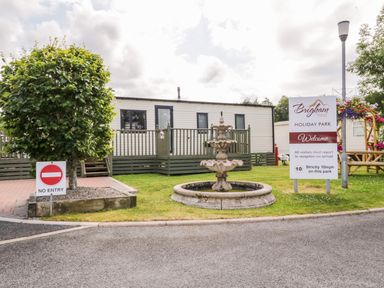 A holiday park with a fountain and welcome sign outside a cabin at Brigham Holiday Park