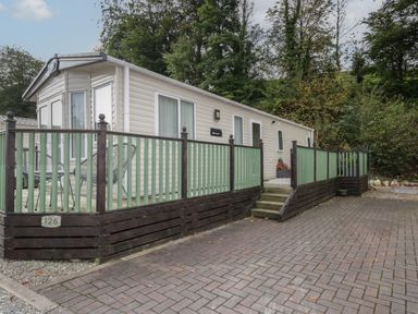A mobile home with green and brown wooden railing and paved driveway surrounded by trees at The Hideaway in Cockermouth