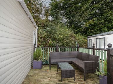 An outdoor deck area with wicker corner sofa and glass top table surrounded by railings and plants at The Hideaway in Cockermouth