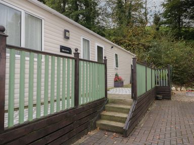 An exterior view of a beige mobile home with green and brown wooden railing and steps leading to the entrance at The Hideaway in Cockermouth