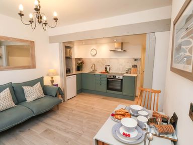 A kitchen and dining area with green cabinets a sofa and a table set with plates cups and pastries at The Riddle in Whitby