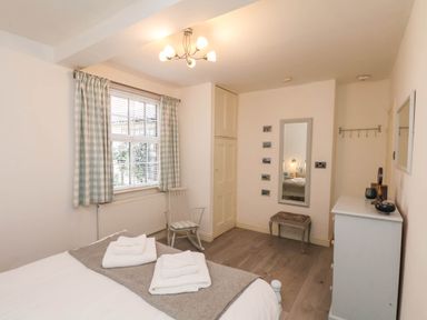 A bedroom with a bed, folded towels, rocking chair, window with curtains, wall mirror, small stool, and white dresser at The Riddle in Whitby