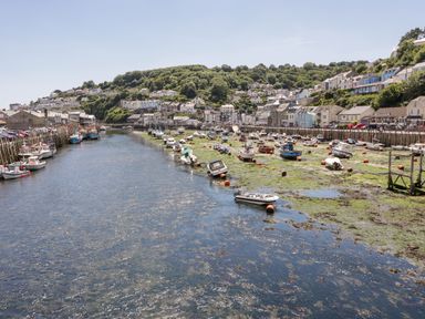 A harbor with boats docked along the water and houses on a hill in the background at 6 Valley View in Lanreath