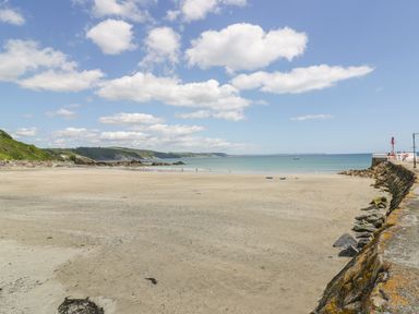 A wide sandy beach with people near the water a stone wall and a red lighthouse at 6 Valley View Lanreath