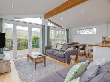 A living room with two sofas coffee table dining table and large windows at 6 Valley View in Lanreath