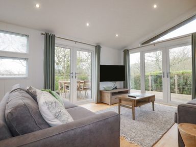 A living room with gray sofas wooden coffee table wall-mounted TV and glass doors opening to a deck at 6 Valley View in Lanreath