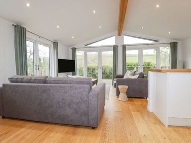 A living room with gray sofas a wooden stool a flat screen tv and large windows at 6 Valley View in Lanreath