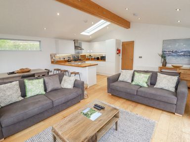 An open plan living area with two sofas a wooden coffee table a dining table and a kitchen at 6 Valley View in Lanreath