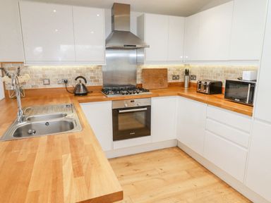 A kitchen with wooden countertops a sink a gas stove an oven a kettle a knife set a toaster and a microwave at 6 Valley View in Lanreath