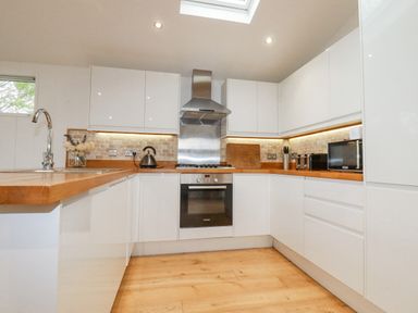 A kitchen with white cabinets wooden countertops a stainless steel oven and hood a kettle toaster microwave and flowers on the counter at 6 Valley View in Lanreath
