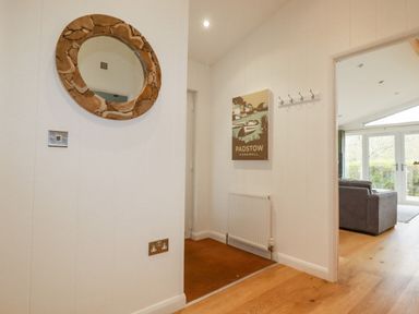 A hallway with a round wooden framed mirror a poster a radiator and an open doorway to a living room at 6 Valley View in Lanreath
