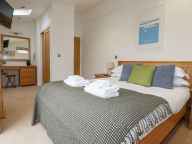 A bedroom with a double bed with cushions and a blanket and folded towels on top with a dressing table and mirror at 6 Valley View in Lanreath