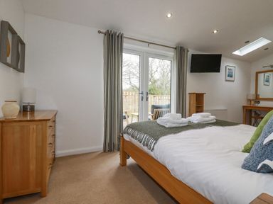 A bedroom with a wooden bed with pillows and folded towels a wooden dresser a TV wall mounted and double glass doors leading outside at 6 Valley View in Lanreath