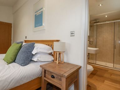A bedroom with a wooden bed green and blue pillows a wooden nightstand with a lamp and an adjacent bathroom with a shower at 6 Valley View Lanreath
