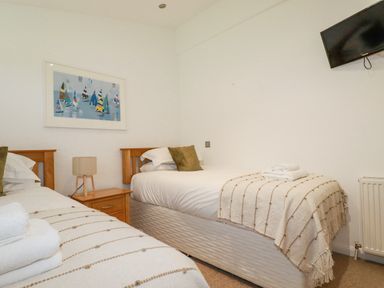 A bedroom with two single beds two pillows a wooden bedside table lamp and a wall mounted television at 6 Valley View in Lanreath