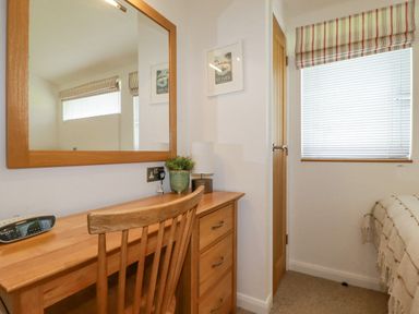 A bedroom corner with wooden desk and chair a large mirror on the wall and a window with blinds at 6 Valley View in Lanreath