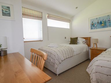 A bedroom with two single beds, a wooden desk and chair, two windows with blinds and striped valances, and framed artwork at 6 Valley View Lanreath