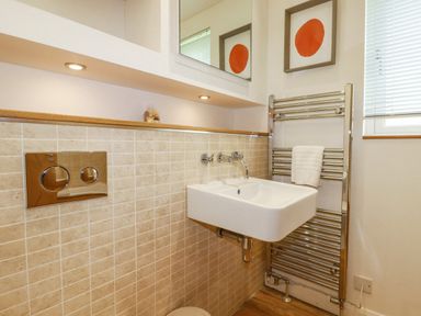 A bathroom with a wall-mounted sink a chrome towel radiator a window with blinds and tiled walls at 6 Valley View in Lanreath