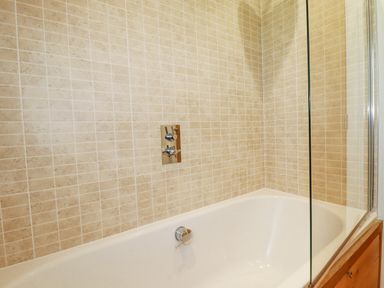 A bathtub with beige tiled walls and a glass shower screen at 6 Valley View in Lanreath