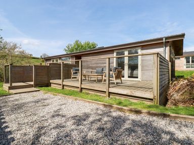 A wooden deck with outdoor chairs and a table in front of a wooden cabin at 6 Valley View in Lanreath