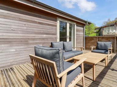 An outdoor patio with wooden chairs and a table in front of a wooden house at 6 Valley View Lanreath