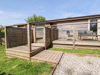 An outdoor wooden deck with chairs and a table next to a building at 6 Valley View in Lanreath
