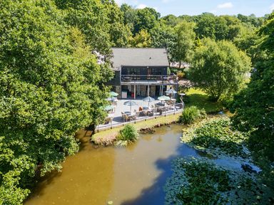 A building with outdoor seating on a deck overlooking a pond surrounded by trees at 6 Valley View in Lanreath