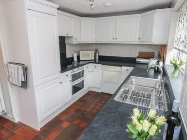 A kitchen with white cabinets black countertops a sink microwave oven and flowers by the window at Ty'r Winllan in Newport Pembrokeshire