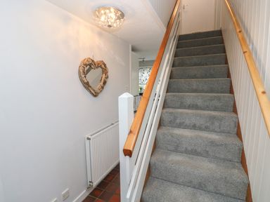 A stairway with grey carpet and wooden handrails next to a white wall with a wooden heart-shaped mirror and a radiator at Ty'r Winllan in Newport Pembrokeshire