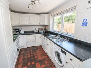 A kitchen with white cabinets black countertops a sink washing machine dishwasher and toaster by a window at Ty'r Winllan Newport Pembrokeshire