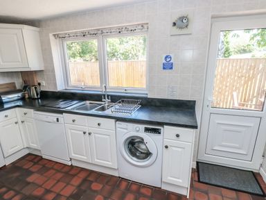 A kitchen with white cabinets a washing machine dishwasher and a window near a door at Ty'r Winllan in Newport Pembrokeshire
