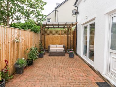 A paved outdoor patio area with a wooden pergola seating area and potted plants at Ty'r Winllan in Newport Pembrokeshire