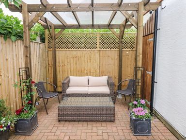 An outdoor seating area with wicker sofa and chairs under a wooden pergola with glass roof at Ty'r Winllan Newport Pembrokeshire