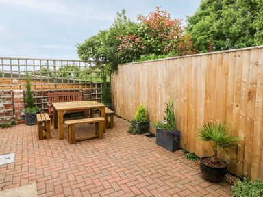 An outdoor patio with wooden table and benches next to a wooden fence with potted plants at Ty'r Winllan in Newport Pembrokeshire