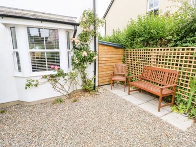A gravel patio area with two wooden chairs near a trellis fence and a rose bush by a white house at Ty'r Winllan in Newport Pembrokeshire