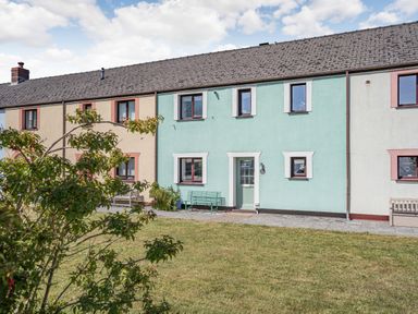 A row of terrace houses with pastel-colored walls a green door and benches with a grassy yard in front at Granary Cottage in Pembroke