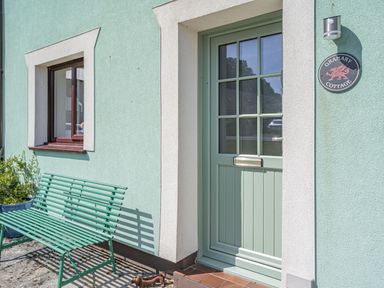 A green bench next to a green door and a window on a light green wall at Granary Cottage in Pembroke
