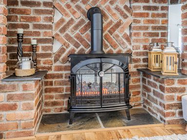 A black wood stove with fire inside surrounded by brick walls with candles and lanterns on shelves at Granary Cottage in Pembroke