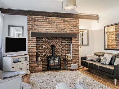 A living room with a brick fireplace a black leather sofa a white TV stand with a television and a large rug at Granary Cottage in Pembroke