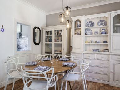 A dining room with a wooden round table set with blue and white plates and glassware surrounded by white chairs with a white cabinet holding blue and white china at Granary Cottage in Pembroke
