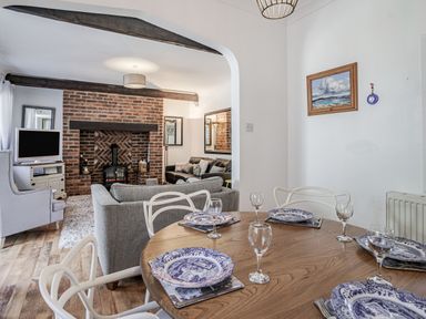 A dining area with a wooden table set with plates and glasses next to a living room with sofas and a brick fireplace at Granary Cottage in Pembroke