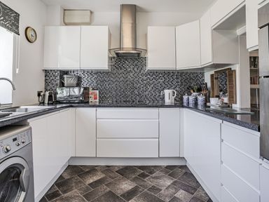 A kitchen with white cabinets black countertops a mosaic tile backsplash a washing machine and various kitchen appliances at Granary Cottage in Pembroke