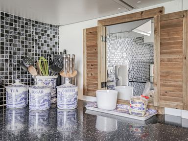 A kitchen counter with containers for tea sugar coffee utensils knives a cup a tray and a small pack of welsh cakes at Granary Cottage in Pembroke