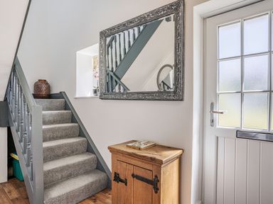 A hallway with carpeted stairs wooden cabinet mirror on the wall and a white door at Granary Cottage in Pembroke