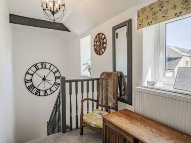 A hallway with a wooden chair a large mirror a wooden chest a window and two wall clocks at Granary Cottage in Pembroke