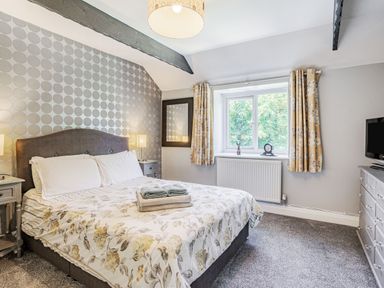 A bedroom with a double bed bedside tables lamps a window with yellow curtains a dresser and a television at Granary Cottage in Pembroke
