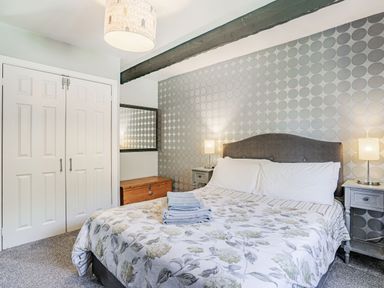 A bedroom with a bed with floral bedding two bedside tables with lamps a wooden chest a mirror and a closet with double doors at Granary Cottage in Pembroke