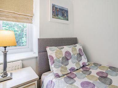 A bedroom corner with a bed with patterned bedding a bedside table with a lamp and a window with a shade at Granary Cottage in Pembroke