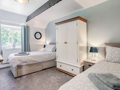 A bedroom with two single beds a white wardrobe a bedside table with a lamp and a window with curtains at Granary Cottage in Pembroke