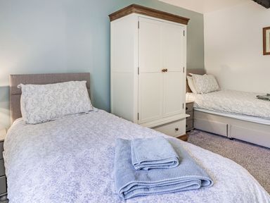 A bedroom with two single beds a white wardrobe and folded towels on one bed at Granary Cottage in Pembroke